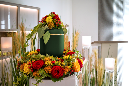 urna otoczona wieńcem kwiatów z żółtymi i czerwonymi kwiatami podczas nabożeństwa pogrzebowego kremacji