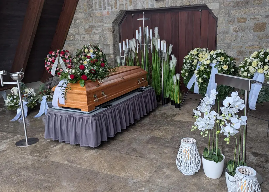 Ein Sarg ist bei einer Erdbestattung mit Blumen dekoriert aufgestellt