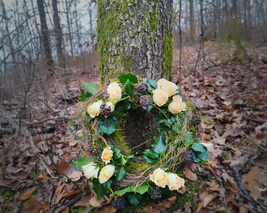 Ein Blumenkranz ist mitten im herbstlichen Wald an einem Baum gelehnt