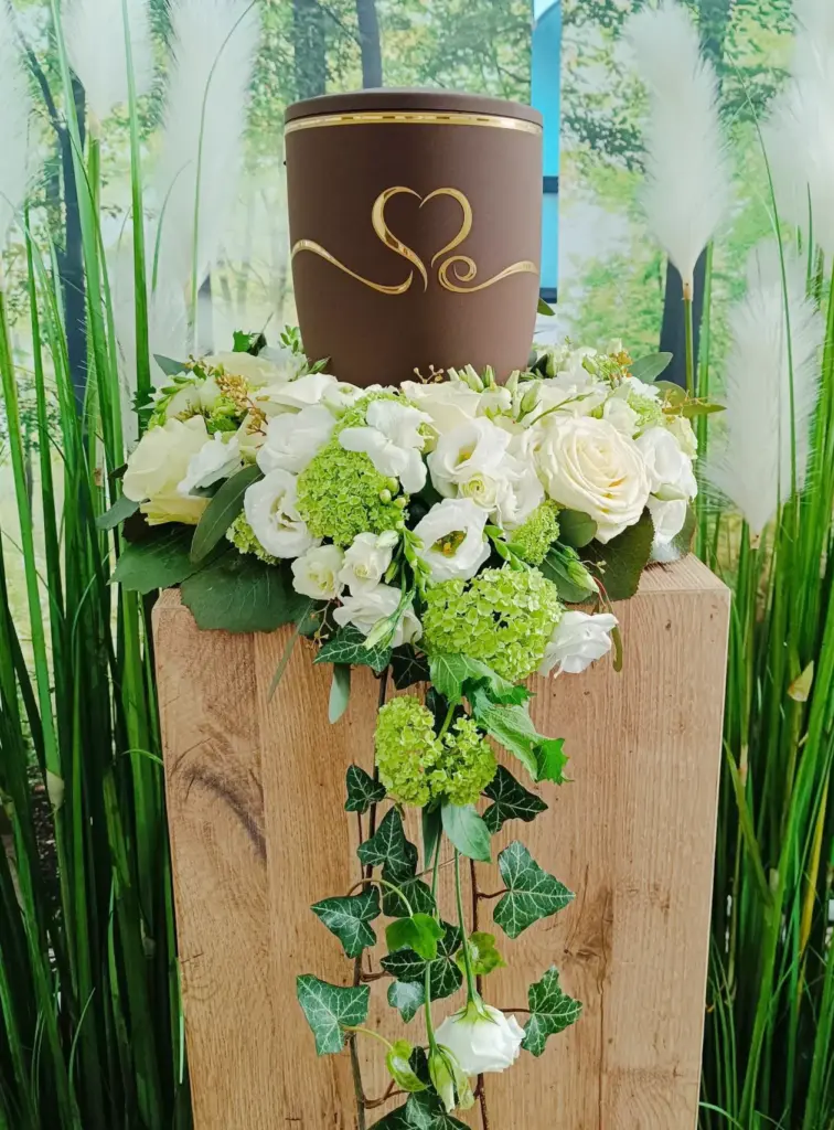 Eine Urne steht mit Blumen dekoriert auf einer Holzstehle