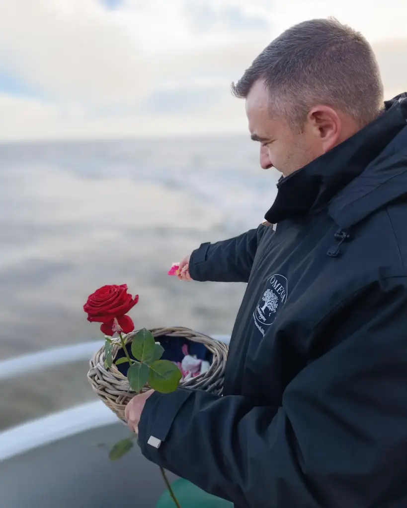 Ein Mann wirft während einer Seebestattung Blumen auf das Wasser
